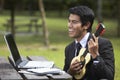 Young Asian businessman playing ukulele in a park. Conceptual image Royalty Free Stock Photo