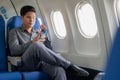 A young Asian businessman sits in a seat near the window talking on his smartphone, Royalty Free Stock Photo