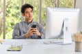 Young asian businessman sitting and using smartphone in the office room with computer desktop, meeting board and accessories Royalty Free Stock Photo