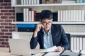 Young Asian businessman wear suit talking on mobile and see paperwork while working with laptop on desk table in modern office. Royalty Free Stock Photo