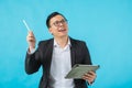 Young Asian businessman wearing glasses holding tablet and thinking about his business idea isolated on blue background.Concept of Royalty Free Stock Photo