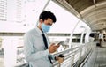 Young Asian Businessman Wearing a Surgical Mask and Using a Smart Phone in City. Healthcare in New Normal Lifestyle Royalty Free Stock Photo