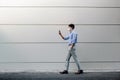 Young Asian Businessman Wearing a Surgical Mask and Using a Smart Phone while Walking by the Urban Building Wall Royalty Free Stock Photo