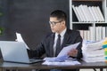 Young asian businessman working with financial data graph document stack on table to analyze financial reporting