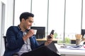 Young Asian businessmen watch smart phones and hold coffee mugs