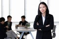 Young Asian businesswoman in black suit standing and posing to camera in office with her team in blur background Royalty Free Stock Photo