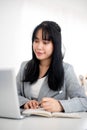 A young Asian businesswoman is looking at her laptop screen while taking notes in the notebook Royalty Free Stock Photo