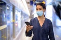 Young Asian businesswoman with mask using phone while waiting at the subway train station Royalty Free Stock Photo