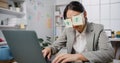 Young Asian businesswoman sitting on desk overworked tired sleep over a laptop at office. Exhausted burnout lady  with two post-it Royalty Free Stock Photo