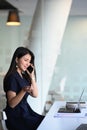 Young Asian businesswoman sitting at her office desk and talking on mobile phone. Royalty Free Stock Photo