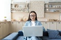 Young asian businesswoman working remotely from home sitting on sofa serious and focused using laptop for online