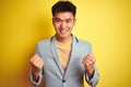 Young asian chinese businessman wearing jacket standing over isolated yellow background celebrating surprised and amazed for Royalty Free Stock Photo