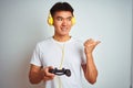 Young asian chinese gamer man playing video game standing over isolated white background pointing and showing with thumb up to the Royalty Free Stock Photo