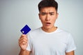 Young asian chinese man holding credit card standing over isolated white background scared in shock with a surprise face, afraid Royalty Free Stock Photo