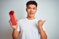 Young asian chinese man holding valentine present standing over isolated white background pointing and showing with thumb up to Royalty Free Stock Photo