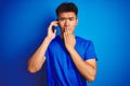 Young asian chinese man talking on the smartphone standing over isolated blue background cover mouth with hand shocked with shame Royalty Free Stock Photo