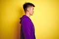 Young asian chinese man wearing purple sweatshirt standing over isolated yellow background looking to side, relax profile pose Royalty Free Stock Photo