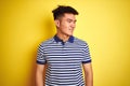 Young asian chinese man wearing striped polo standing over isolated yellow background looking away to side with smile on face, Royalty Free Stock Photo