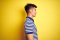 Young asian chinese man wearing striped polo standing over isolated yellow background looking to side, relax profile pose with Royalty Free Stock Photo