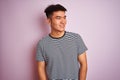 Young asian chinese man wearing striped t-shirt standing over isolated pink background looking away to side with smile on face, Royalty Free Stock Photo