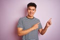 Young asian chinese man wearing striped t-shirt standing over isolated pink background smiling and looking at the camera pointing Royalty Free Stock Photo