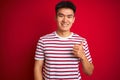 Young asian chinese man wearing striped t-shirt standing over isolated red background doing happy thumbs up gesture with hand Royalty Free Stock Photo