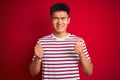 Young asian chinese man wearing striped t-shirt standing over isolated red background excited for success with arms raised and Royalty Free Stock Photo