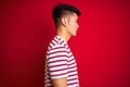 Young asian chinese man wearing striped t-shirt standing over isolated red background looking to side, relax profile pose with Royalty Free Stock Photo