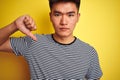 Young asian chinese man wearing striped t-shirt standing over isolated yellow background with angry face, negative sign showing Royalty Free Stock Photo