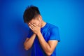 Young asian chinese man wearing t-shirt standing over isolated blue background with sad expression covering face with hands while Royalty Free Stock Photo