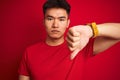 Young asian chinese man wearing  t-shirt standing over isolated red background with angry face, negative sign showing dislike with Royalty Free Stock Photo