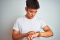 Young asian chinese man wearing t-shirt standing over isolated white background Checking the time on wrist watch, relaxed and Royalty Free Stock Photo