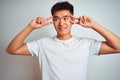 Young asian chinese man wearing t-shirt standing over isolated white background Doing peace symbol with fingers over face, smiling Royalty Free Stock Photo