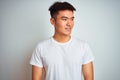 Young asian chinese man wearing t-shirt standing over isolated white background looking away to side with smile on face, natural Royalty Free Stock Photo