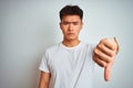 Young asian chinese man wearing t-shirt standing over isolated white background looking unhappy and angry showing rejection and Royalty Free Stock Photo