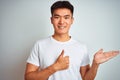 Young asian chinese man wearing t-shirt standing over isolated white background Showing palm hand and doing ok gesture with thumbs Royalty Free Stock Photo