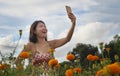 Young Asian Chinese tourist woman taking self portrait selfie photo with mobile phone on excursion through beautiful flowers field Royalty Free Stock Photo