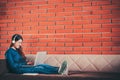 Young Asian college student girl using laptop computer, headphone, smartphone, notebook on couch sofa, sit at university campus Royalty Free Stock Photo