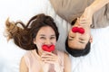 Young asian couple laying down in opposite direction together kissing red heart shape pillows on white sheet bed happily Royalty Free Stock Photo