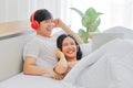 Young Asian couple lying in bed watching and laughing over comedy movie together Royalty Free Stock Photo