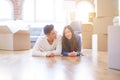 Young asian couple lying on the floor of new house arround cardboard boxes relaxing and smiling happy Royalty Free Stock Photo