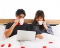 Young Asian couple sitting on bed drinking coffee and looking at computer Royalty Free Stock Photo