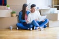 Young asian couple sitting on the floor of new house arround cardboard boxes using laptop and drinking a cup of coffee Royalty Free Stock Photo