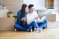 Young asian couple sitting on the floor of new house arround cardboard boxes using laptop and drinking a cup of coffee Royalty Free Stock Photo