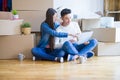 Young asian couple sitting on the floor of new house arround cardboard boxes using laptop and drinking a cup of coffee Royalty Free Stock Photo