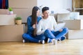 Young asian couple sitting on the floor of new house arround cardboard boxes using laptop and drinking a cup of coffee Royalty Free Stock Photo