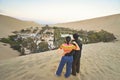 A young asian couple stand on the desert and enjoy the view of Huacachina, Ica, Peru.