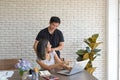 Young asian couple wear casual clothing relaxing while sitting at big wooden table in modern kitchen and working with laptop Royalty Free Stock Photo