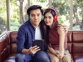 Young Asian couple wearing headphone sitting close together on couch in living room at home , a man hug his girlfriend holding Royalty Free Stock Photo