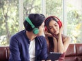 Young Asian couple wearing headphones sitting close together on couch in living room , a woman enjoy listening music, a man Royalty Free Stock Photo